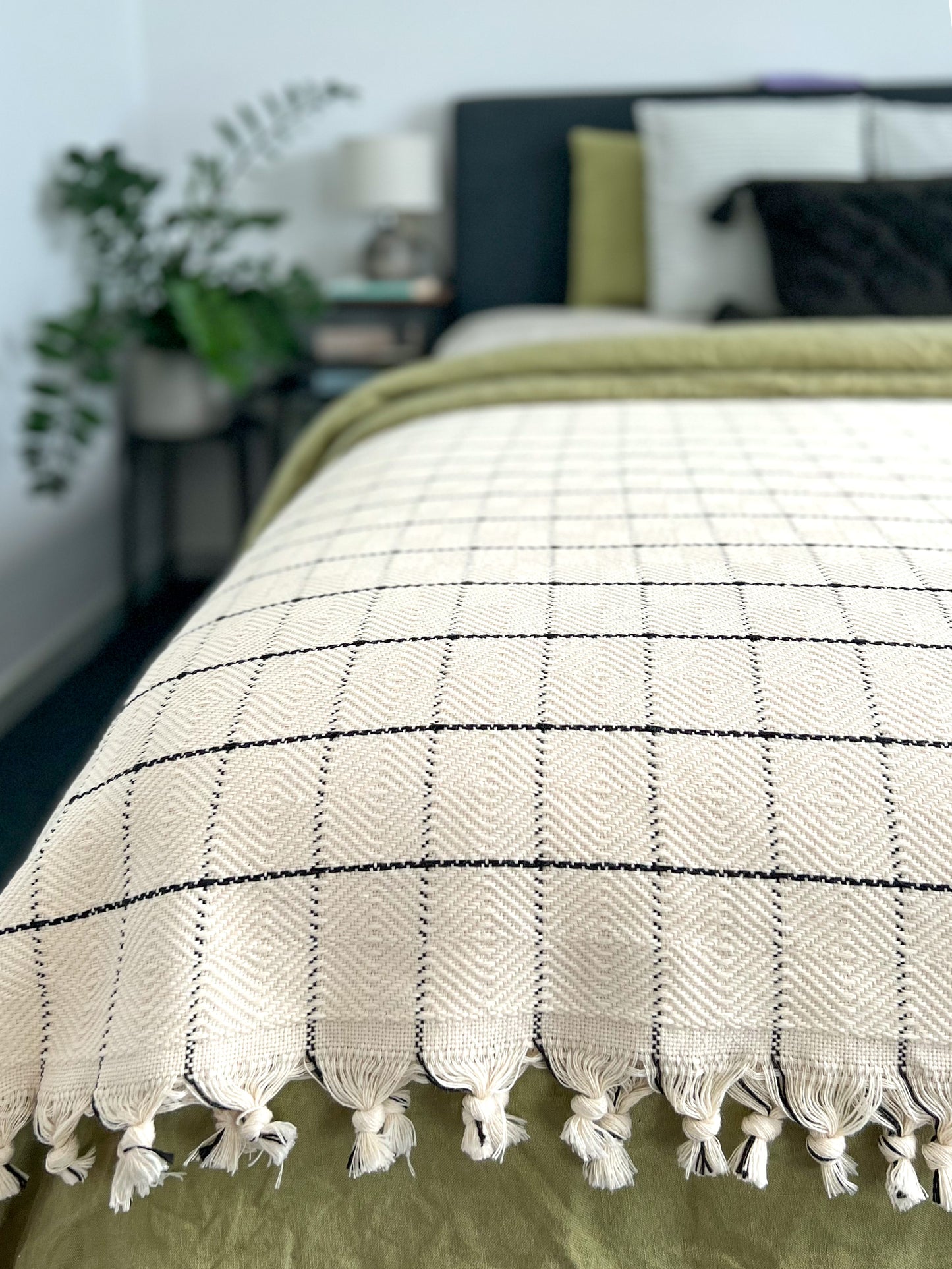 Cream handwoven cotton throw blanket with windowpane pattern on a bed, enhancing home decor with timeless comfort.