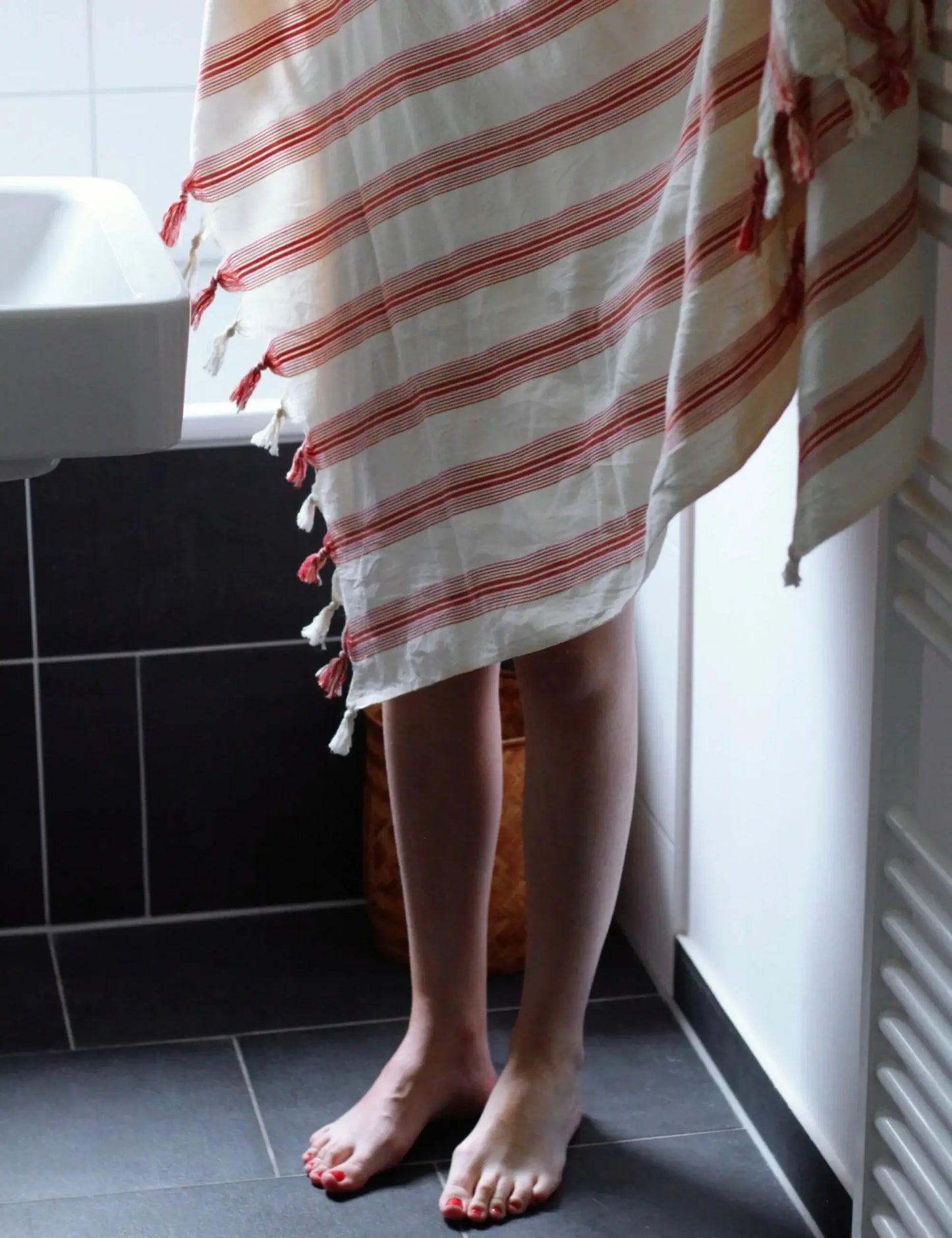 Person wrapped in Ruby Handwoven Hammam Towel with red stripes, showcasing its vibrant design and lightweight cotton fabric.