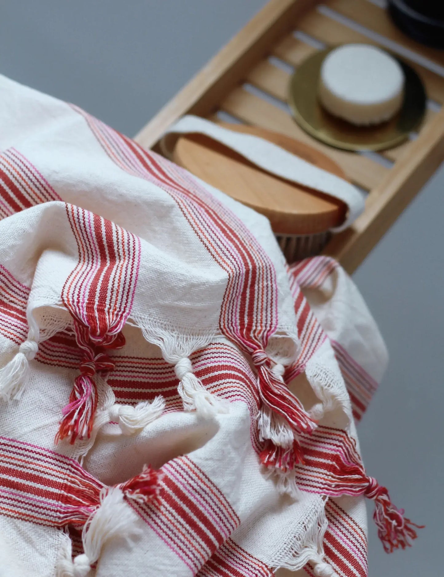 Ruby handwoven hammam towel with red stripes, showcasing artisanal peshtemal design, draped over a wooden bath rack.