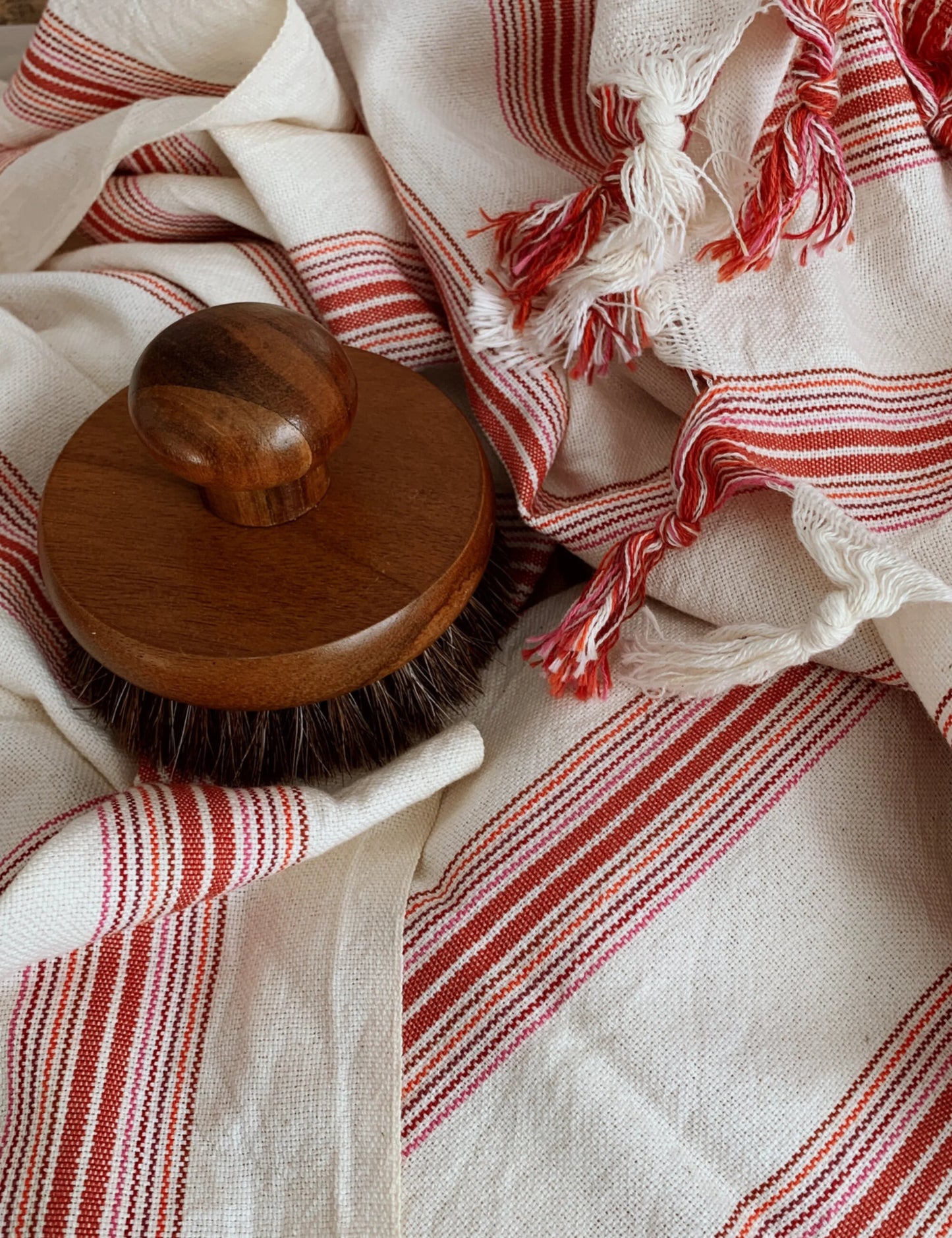 Ruby handwoven hammam towel with red stripes and wooden brush, perfect as cotton peshtemal for beach, sauna, or bath use.