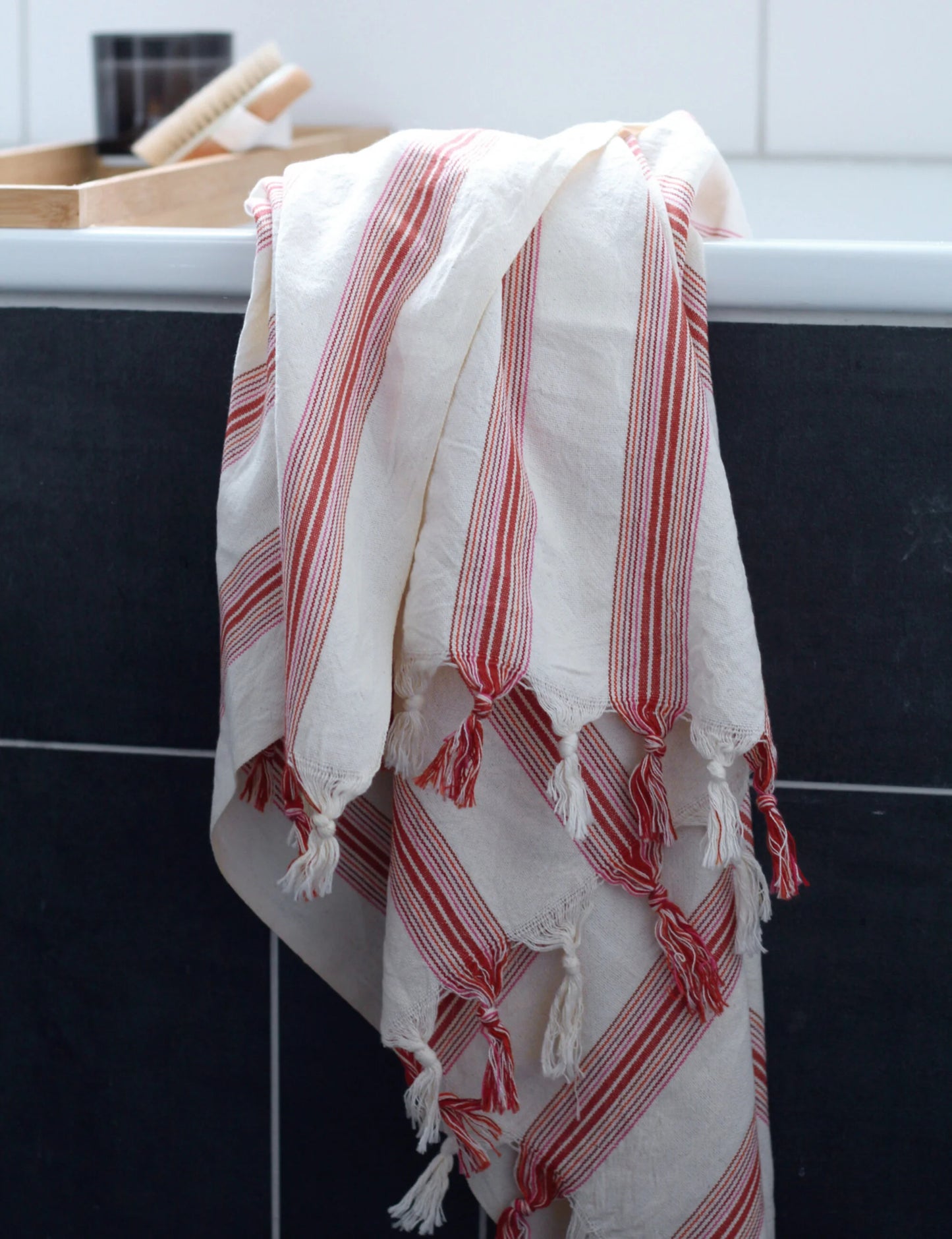 Ruby handwoven hammam towel with red stripes, perfect as a cotton, beach, or sauna towel, elegantly draped over a bathtub.