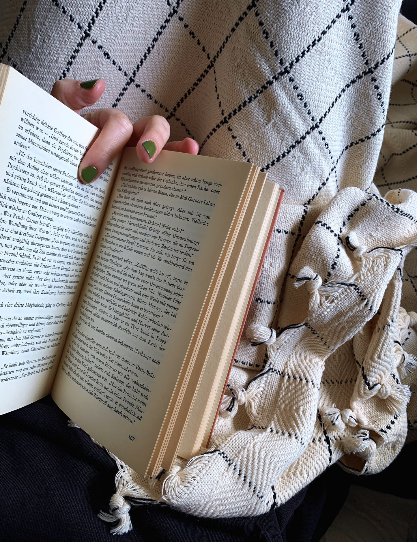 Person holding a book on a sofa draped with a Pia Turkish cotton throw blanket in a classic windowpane pattern.
