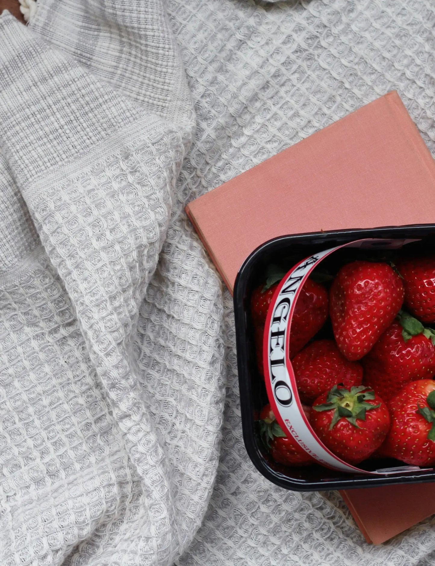Waffle weave gray hammam towel with a box of fresh strawberries on a pink book.